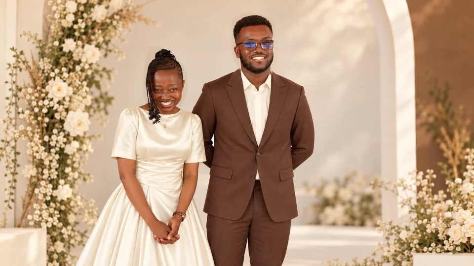 Timothy and Aziza beneath a studio arch, wearing ivory and espresso outfits.