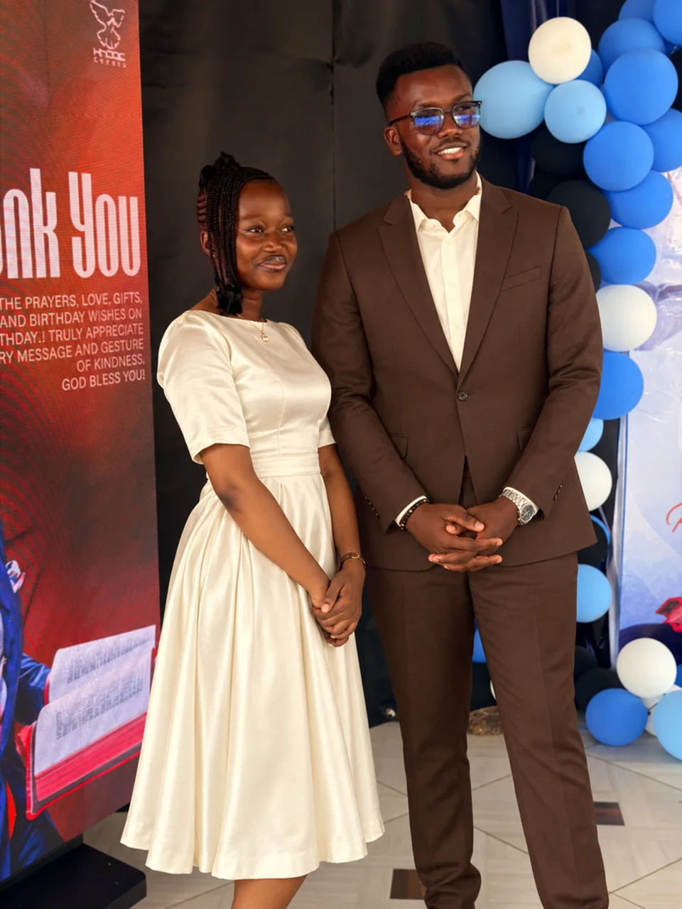 Timothy and Aziza posing together with their hands in front, wearing ivory and espresso outfits.