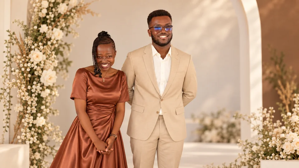 Timothy and Aziza beneath a studio arch, wearing terracotta and champagne outfits.