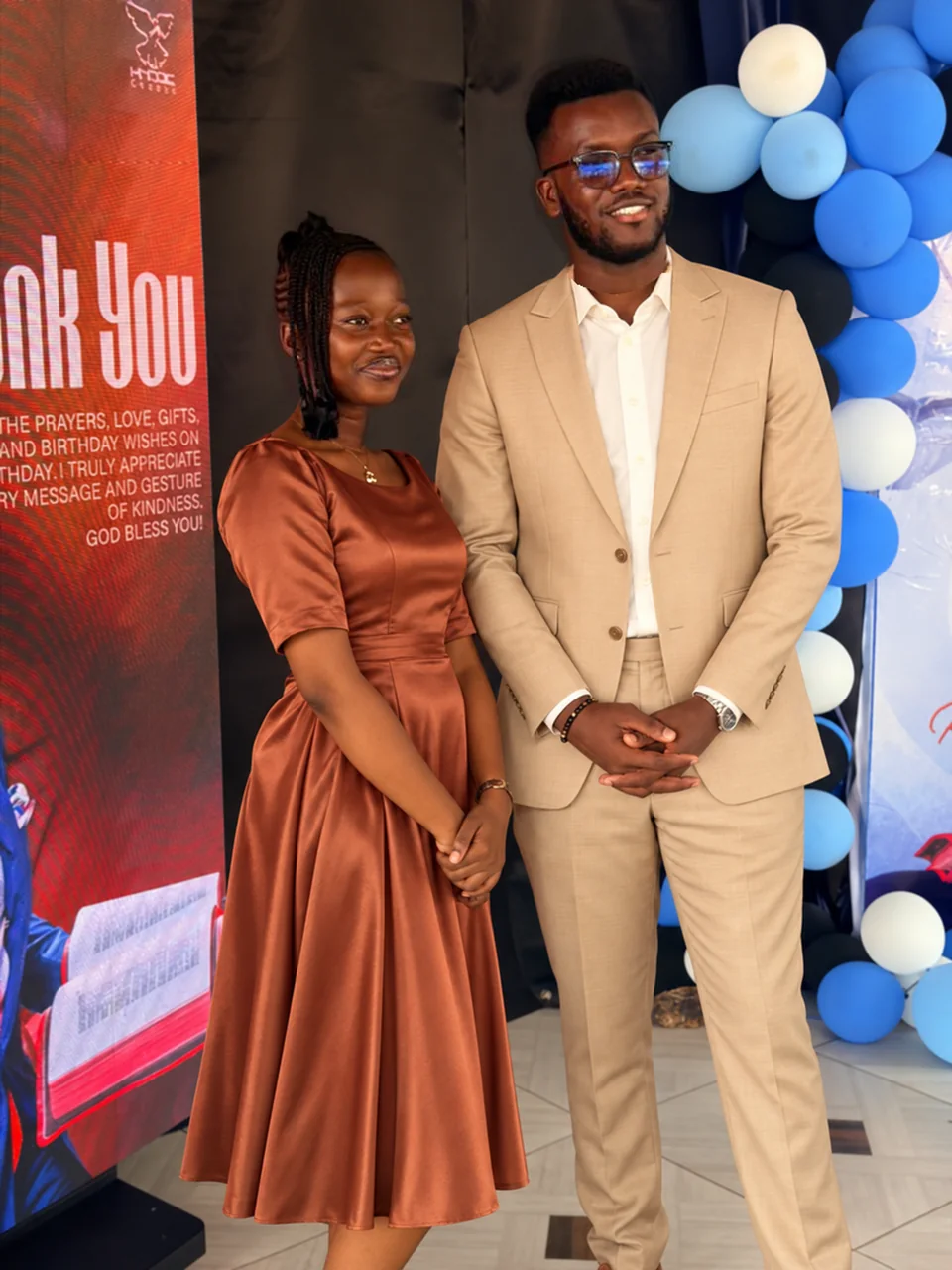 Timothy and Aziza posing together with their hands in front, wearing terracotta and champagne outfits.